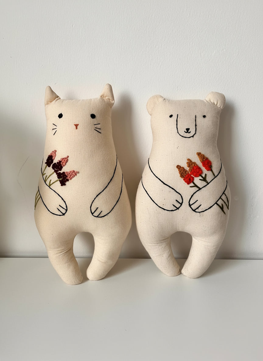 Two plush toys, one cat-like and one bear-like, holding flowers on a white background