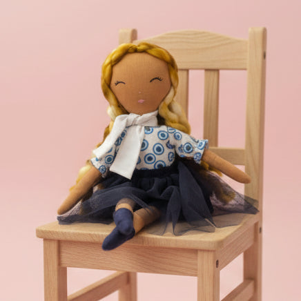 Handmade doll with blonde hair, blue dress, and white collar on a white surface.