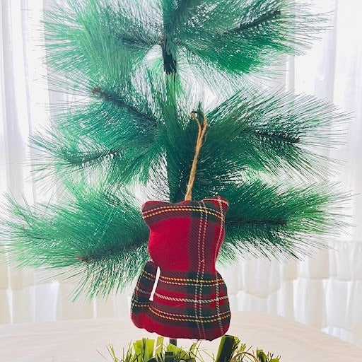 Red plaid Christmas ornaments hanging from a green wreath on a white background